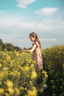 A young girl in a striped dress enjoys a peaceful moment in a blooming yellow flower field. She