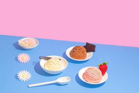 Various flavors of ice cream in white dishes, presented against a striking pink and blue