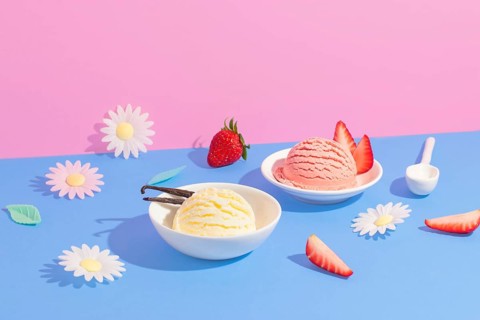 Vanilla and strawberry ice cream in white bowls amid colorful paper flowers on a pink and blue