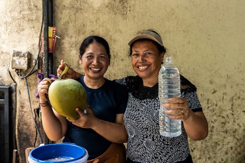 Two smiling asian women showcase a freshly opened coconut and a bottle of coconut water,