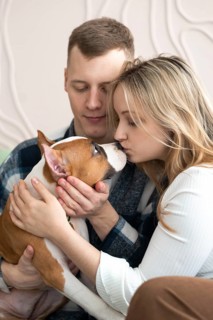 A man and woman affectionately interact with their brown and white dog in a cozy home setting,