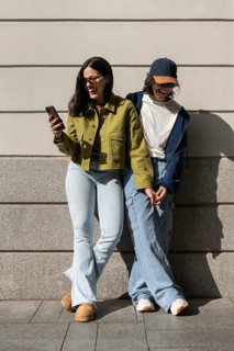 A joyful lesbian couple stands against a wall, holding hands and sharing laughter. The sunny day
