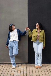 A joyful lesbian couple stands side by side, holding hands and smiling brightly while leaning