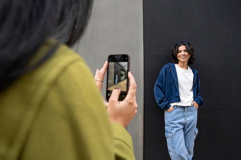 A lesbian couple enjoys a casual outdoor photoshoot. One woman wears denim and smiles against a