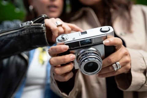 A lesbian couple shares a moment of connection through photography. Their hands hold a vintage