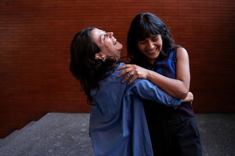 A joyful scene captures a multiethnic lesbian couple embracing and laughing together, celebrating