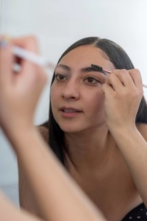 A woman concentrates while applying makeup using a brush in front of a mirror. The close up