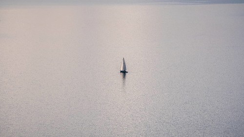 A solitary sailboat on the tranquil waters of Lake Geneva during a sunny winter day, with the snowy