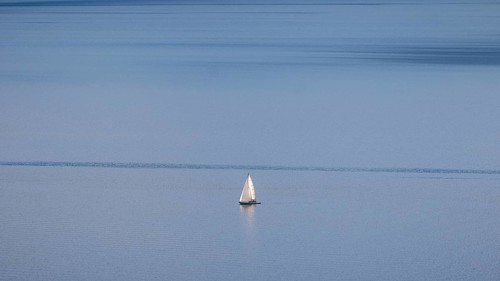A lone sailboat glides over Lake Geneva on a clear winter's day, framed by the vineyards of Lavaux