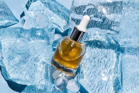 A serum bottle with a dropper is elegantly placed amidst scattered ice cubes, showcasing a