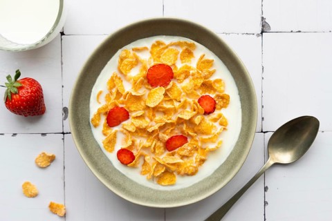 A bowl of crunchy cornflakes with fresh strawberry slices, served in milk. A wholesome breakfast