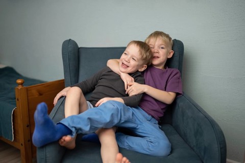Two joyful young brothers share a warm embrace on a cozy blue armchair, radiating happiness and