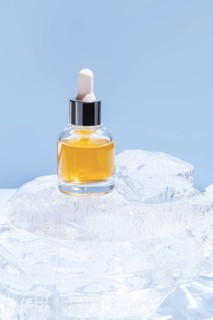 A single cosmetic serum bottle with a dropper cap, presented on a stack of clear ice cubes, under a
