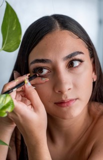 A woman applies eyeliner with precision, focusing intently. Her delicate hand grips the pencil,