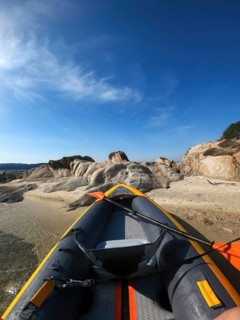 Inflatable kayak resting on a sandy shore in Greece. The vibrant kayak contrasts beautifully with