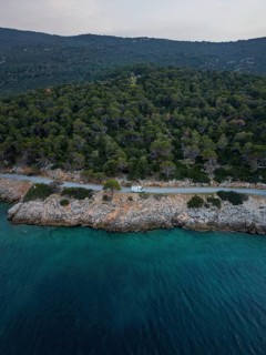Aerial view of a van in a coastal road running through lush green forest by a turquoise sea in