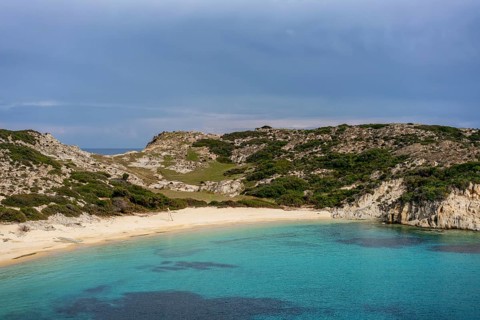 Kalamitsi Beach in Greece offers a serene setting with turquoise waters, golden sand, and a rugged,
