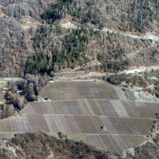 A breathtaking aerial view of Swiss farmland with neatly arranged fields against a rugged hillside.