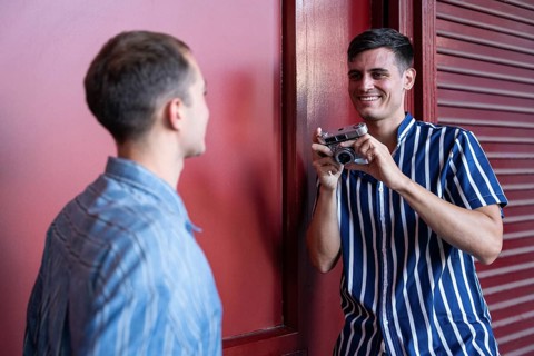Playful gay couple sharing a fun moment during a photo session with a vintage camera. Smiling and
