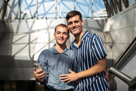 Gay couple smiling and enjoying a sunny day on the streets of Madrid, celebrating pride and love.