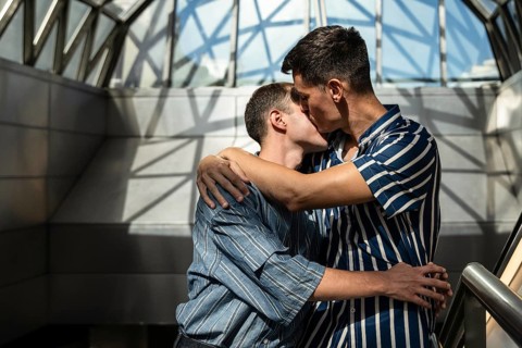 Romantic gay couple embracing and sharing a kiss in a modern architectural setting. Soft light and