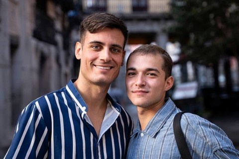 A smiling gay couple enjoys a sunny day while strolling through the lively streets of Madrid. The