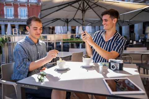 Gay couple enjoying coffee at an outdoor cafe in Plaza Mayor, Madrid. One stirs his coffee while
