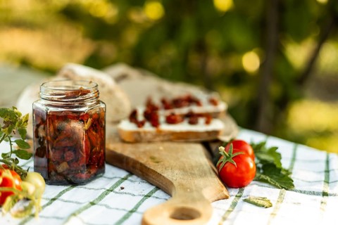 A rustic scene of canapes being prepared. Fresh tomatoes, a jar of preserved vegetables, and bread