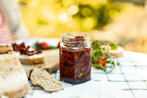 A rustic outdoor setting featuring a jar of homemade sun-dried tomatoes, fresh bread, and ripe