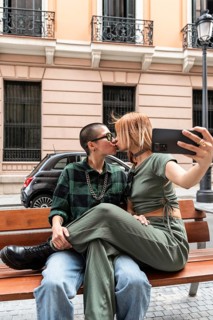 Colombian lesbian couple captures a loving kiss on a city bench, showcasing affection and identity.