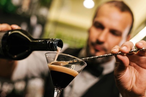 A skilled bartender expertly pours a drink into a glass, showcasing precision and flair. The