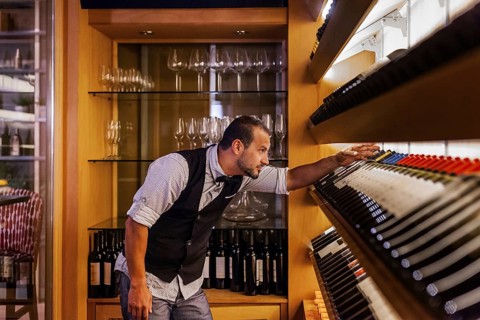 A professional sommelier meticulously selects wine bottles in a sophisticated cocktail bar,