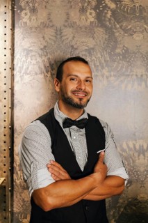 A professional bartender in a stylish cocktail bar setting, dressed in a bow tie and vest, exuding