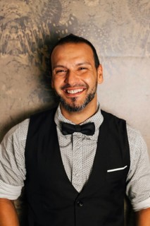 A professional bartender dressed stylishly with a bow tie, smiling warmly. The image captures the