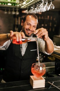 A professional bartender skillfully pours a vibrant cocktail into a glass at a stylish modern bar,