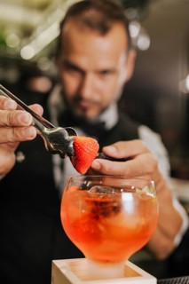 A skilled bartender adds a strawberry garnish to a vibrant cocktail, showcasing his expertise in