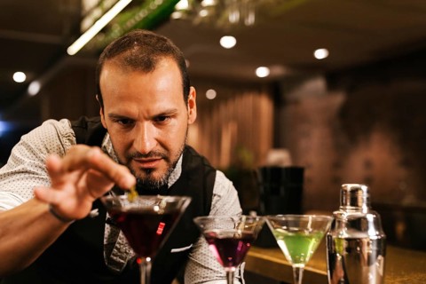 A professional bartender expertly prepares colorful cocktails in a vibrant bar. Focused and