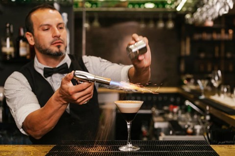 A skilled bartender carefully prepares a sophisticated cocktail at a trendy bar, showcasing expert