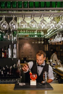 A professional bartender skillfully prepares a vibrant cocktail at an elegant urban bar, surrounded