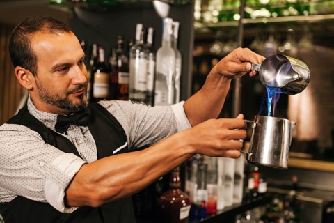 A professional bartender skillfully mixes a colorful cocktail in a chic cocktail bar, demonstrating