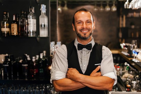 A professional bartender stands confidently in a stylish cocktail bar, surrounded by a selection of