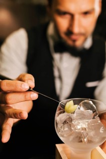 A professional bartender skillfully prepares a cocktail at an elegant bar. Focused on garnishing,