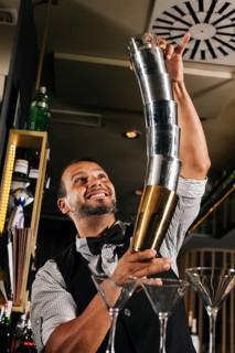 A professional bartender skillfully performs with cocktail shakers in a stylish bar. His expert