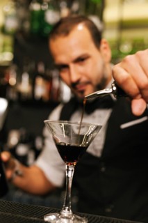 A professional bartender skillfully pours a dark liquid into a martini glass amidst an elegant