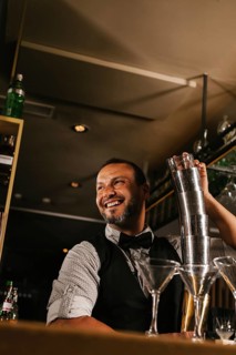A skilled bartender joyfully mixes cocktails at an elegant bar, showcasing expertise and charm.