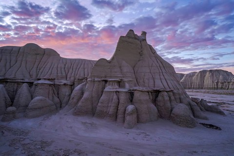 Sunset casts a soft glow over the dramatic and weathered sandstone formations of the