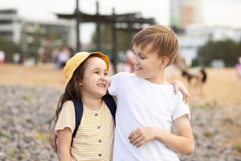 A brother and sister share a joyful moment on a pebble beach. The older boy lovingly wraps his arm