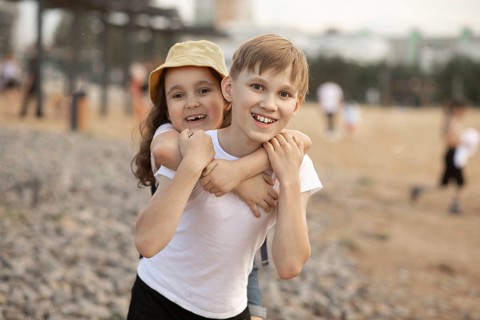 Two joyful siblings, a boy and a girl, share a playful moment outdoors. The girl gives a piggyback