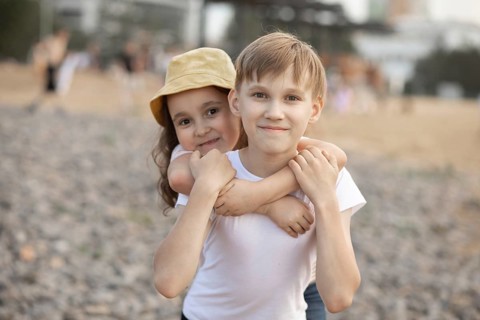 A young boy and his little sister share a warm embrace while smiling at the camera. Their bond and