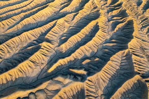 An aerial view of Caineville Mesa's golden desert textures in Utah at sunset. The rippled landscape